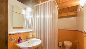 Un baño con un lavamanos blanco, un espejo, una cortina de ducha a rayas y una pared de azulejos naranjas.