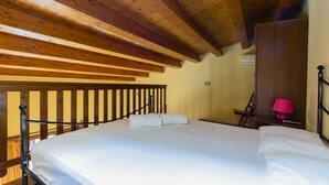 A bedroom with a wooden ceiling, a bed with white bedding, a red lamp on a bedside table, and a wooden ladder against the wall. - Visitsicilia 6 Le Magnole 6 (Castellammare del Golfo)