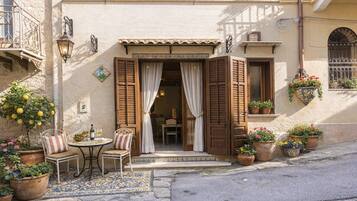 A building with a tiled entrance, a small outdoor seating area with chairs and a table, and potted plants.