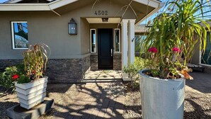 A house with a number '4502' above the door, a front porch, and two large planters with plants. - Arcadia Bright and Cheery House (Phoenix)