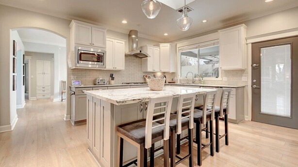 A modern kitchen with white cabinetry, a central island with bar stools, a microwave, and a large window. - Arcadia Bright and Cheery House (Phoenix)