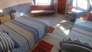 Una camera da letto con due letti, una scrivania e una sedia. Si vede una finestra con tende e una porta.
