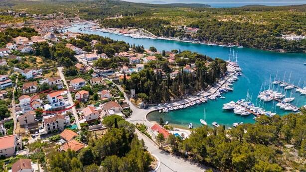 An aerial view of a coastal town with a marina, residential buildings, and surrounding greenery. - Villa Milna Bay, heated pool, Milna, Brač Island (Milna)