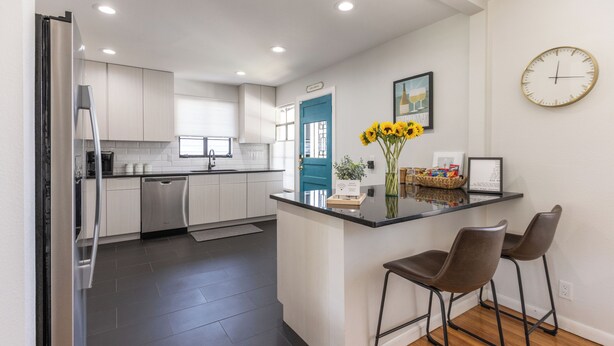 A modern kitchen with white cabinets, a blue door, and a bar area with two stools. - Second Floor Serenity in a Great Location! (San Antonio)