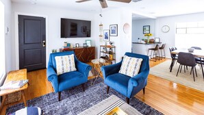 A modern living room with a blue sofa set, a ceiling fan, a flat-screen TV, and a dining area with a table and chairs. - Second Floor Serenity in a Great Location! (San Antonio)