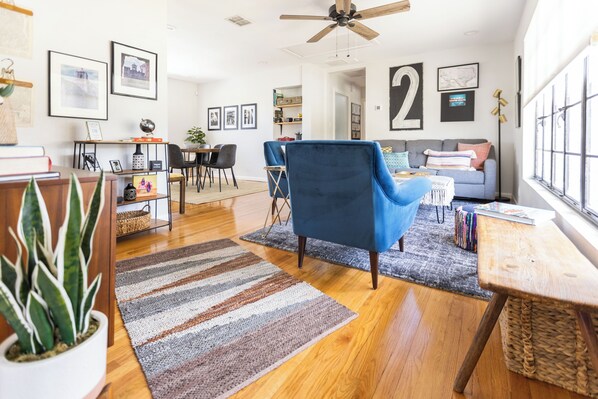 Een ruime woonkamer met een blauwe fauteuil, een houten salontafel en een groot raam met uitzicht.