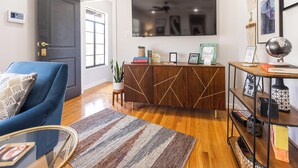 A modern living room with a blue armchair, a wooden cabinet, a flat-screen TV, and a globe on a side table. - Second Floor Serenity in a Great Location! (San Antonio)