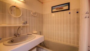Ein Badezimmer mit Waschbecken, Spiegel und Badewanne. An der Wand befinden sich Handtuchhalter und ein gerahmtes Bild über der Badewanne.