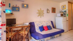 Ein gemütliches Wohnzimmer mit einer Couch, einem Esstisch mit Stühlen, einem Fernseher und einem Kühlschrank.