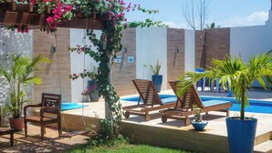 A poolside area with wooden lounge chairs, potted plants, and a clear blue swimming pool. - Pousada Vila de Charme (Barreirinhas)