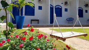 A building with blue doors and windows, a swing, and a garden with red flowers. - Pousada Vila de Charme (Barreirinhas)