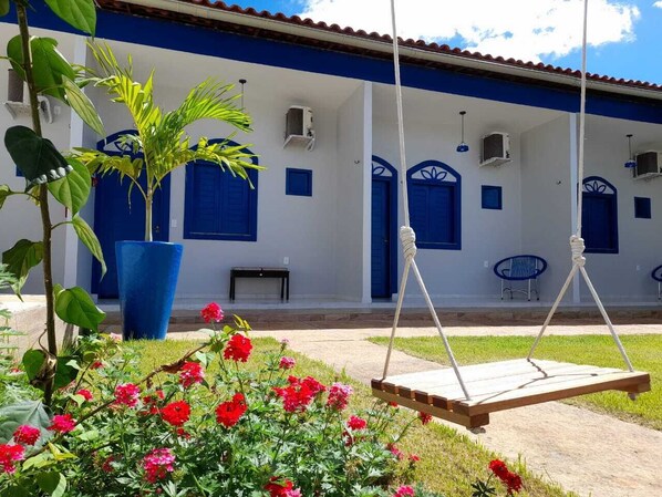 Un edificio con puertas y ventanas azules, una hamaca y un jardín lleno de flores rojas.