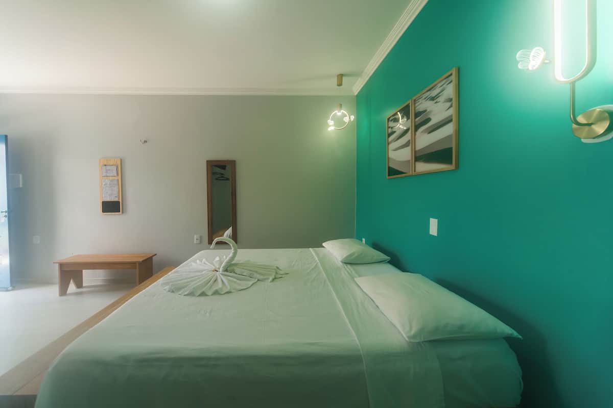 Un dormitorio con cama, una banca, una lámpara de pared y un cuadro enmarcado.