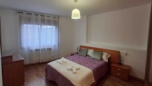 Ein Schlafzimmer mit Bett, Nachttisch, Kommode und einem Fenster mit Vorhängen.