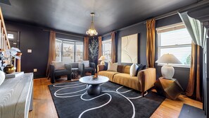Ein modernes Wohnzimmer mit dunkler Farbgestaltung, ausgestattet mit einer Couch, Sesseln, einem Couchtisch und einer Pendelleuchte.