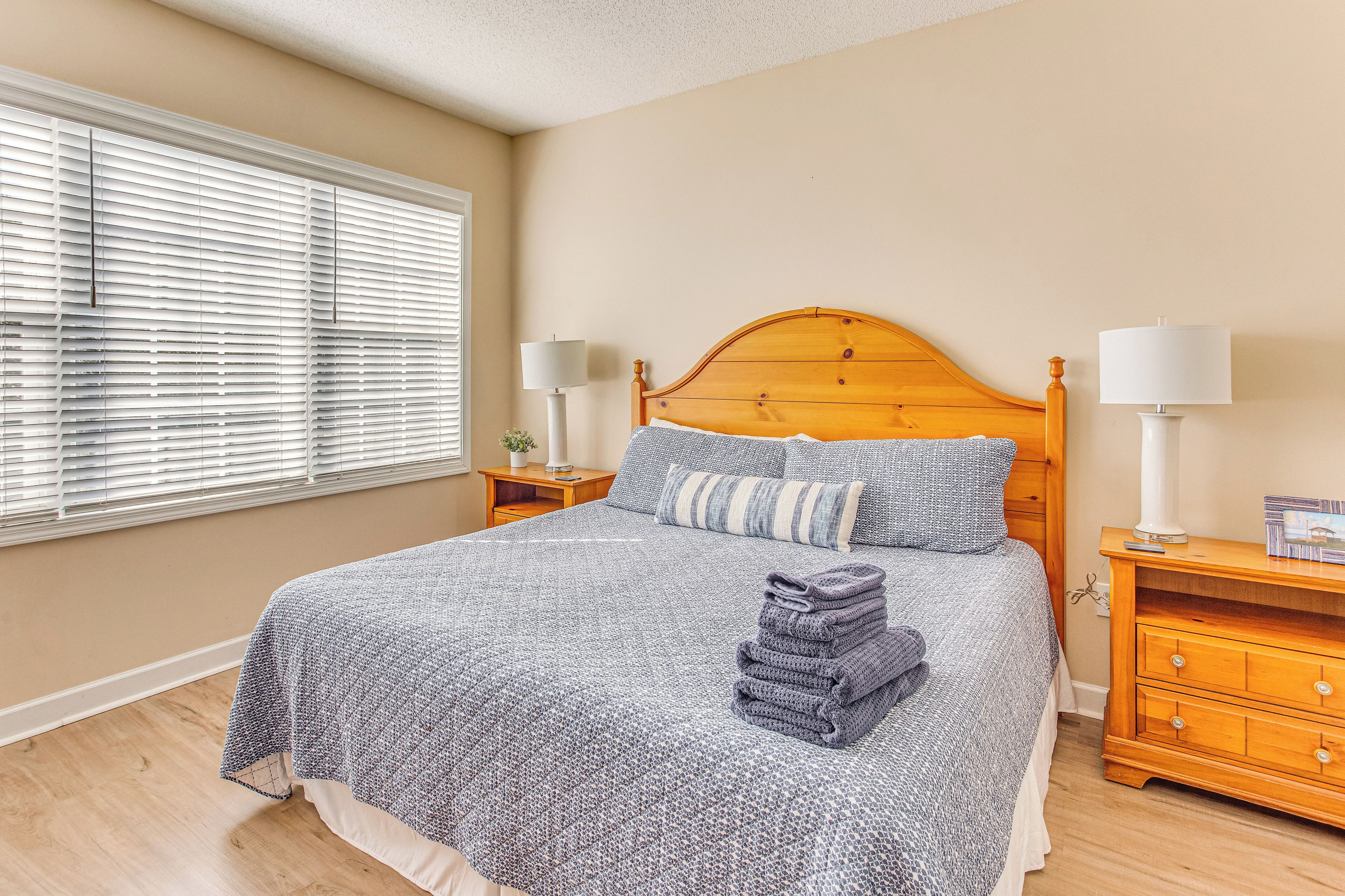 A neatly made bed with a patterned bedspread, two pillows, and a stack of folded towels.