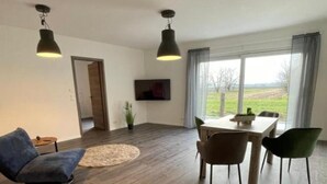 Amplia sala de estar con una mesa de comedor, dos sillas, un sofá y un televisor montado en la pared.