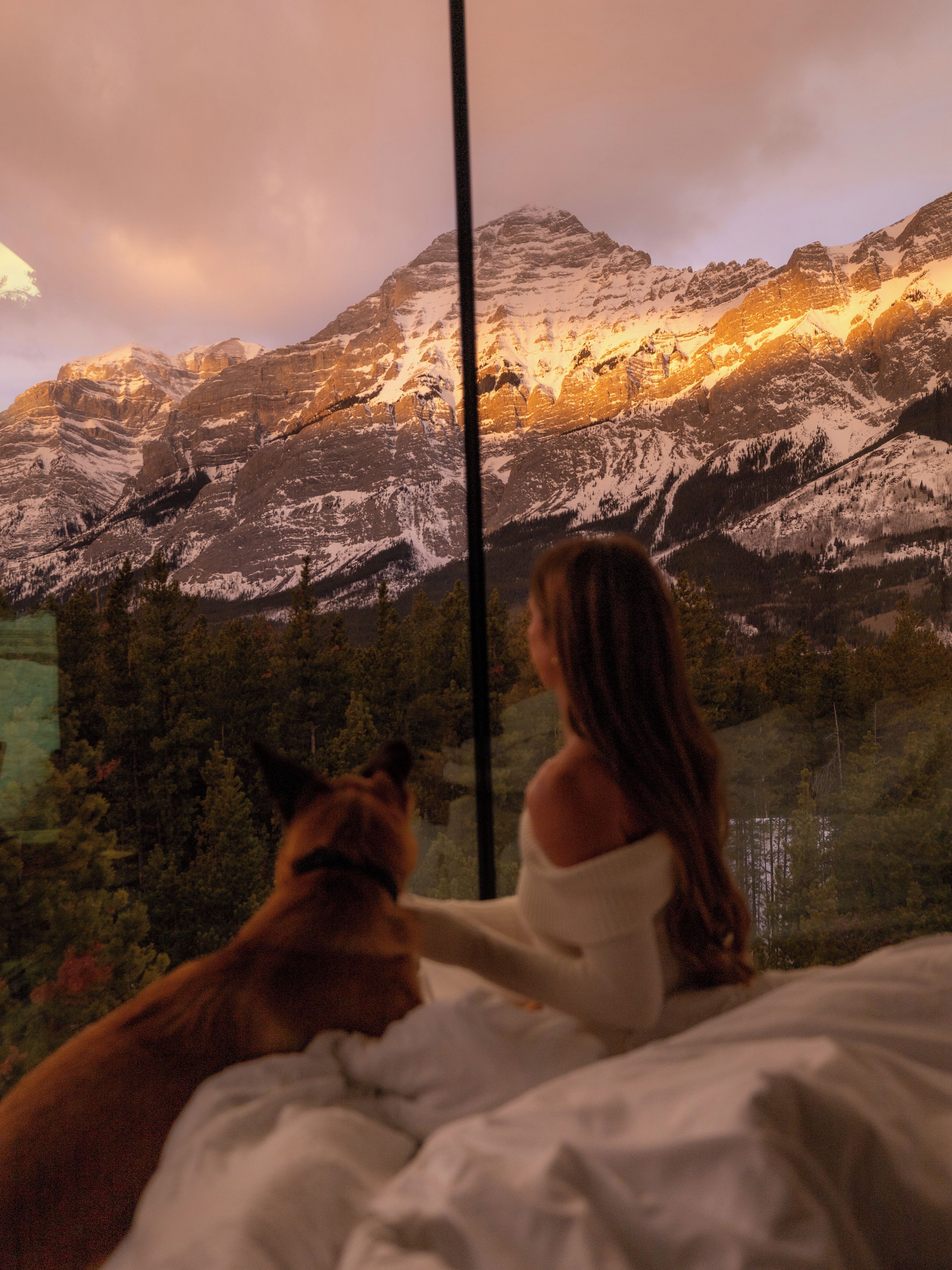 A person sitting on a bed with a mountain view through a window.