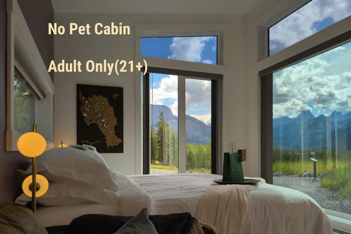 Ein Schlafzimmer mit einem großen Fenster und Blick auf die Berge, einem Bett mit weißer Bettwäsche und einer grünen Tasche auf der Fensterbank.