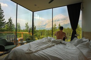 A bedroom with a large window, a bed, a chair, and a small table. - Skyridge Glamping (Kananaskis Village)
