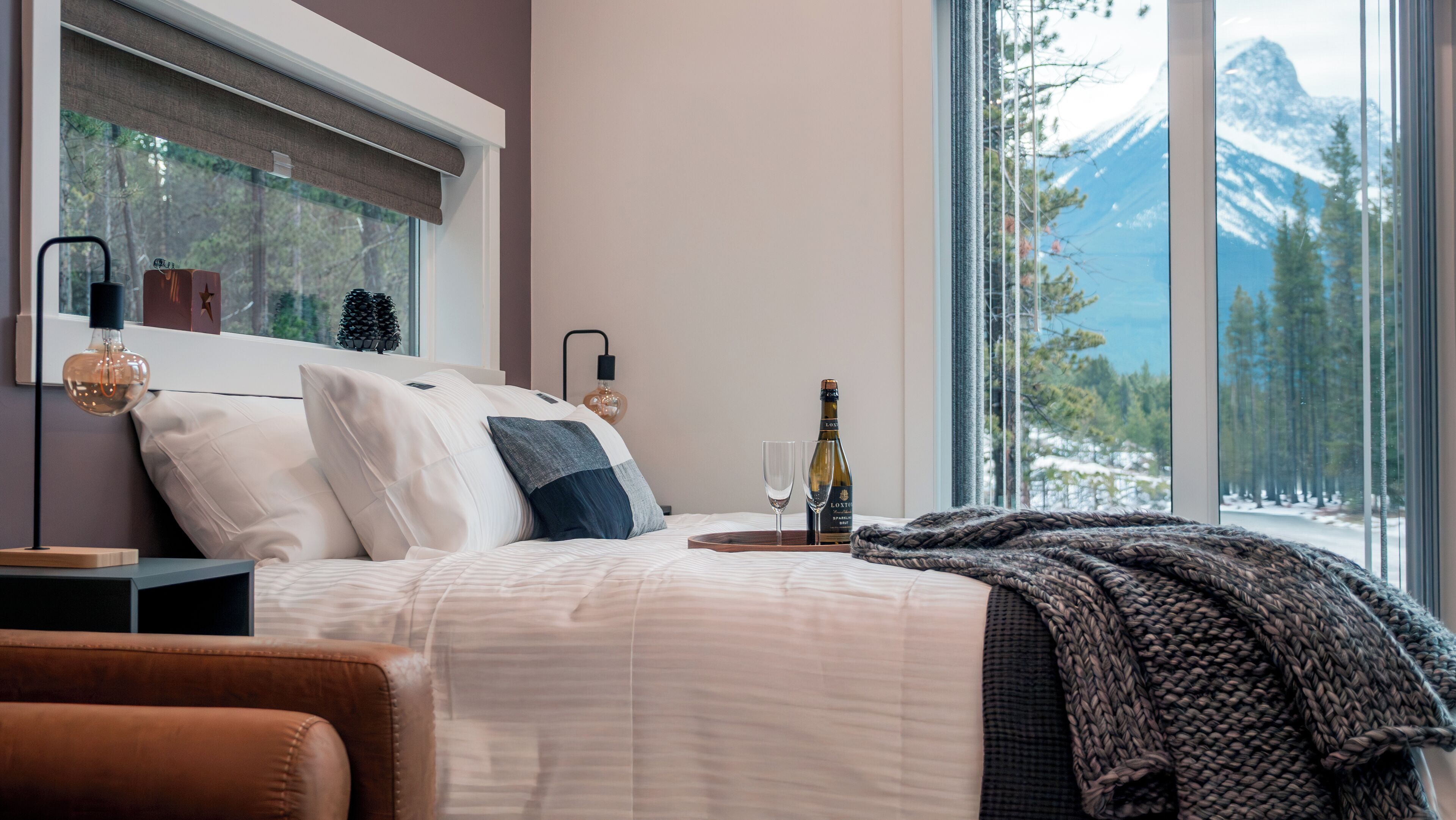Quarto com cama, mesa de cabeceira e janela com vista para uma montanha nevada.
