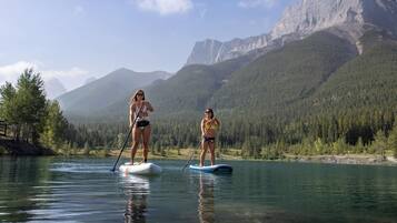 Duas pessoas praticam paddleboarding em um lago calmo, com montanhas ao fundo.