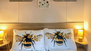 A bed with two pillows featuring a bee design, a bedside table with a lamp, and a wall-mounted artwork above the bed. - 3 bedroom accommodation in Hawick (Hawick)