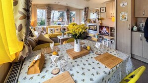 A cozy living room with a sofa, a dining table with a floral tablecloth, and a kitchen area with a refrigerator and cabinets. - 3 bedroom accommodation in Hawick (Hawick)