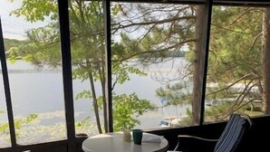 Una habitación con un ventanal grande que da a un lago, una mesa redonda con una taza y dos sillas.