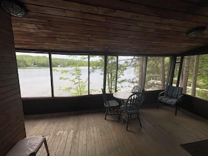 Un espace extérieur aménagé, abrité et doté d’une table et de chaises, de grandes fenêtres donnant sur un plan d’eau et d’un revêtement de sol en bois.