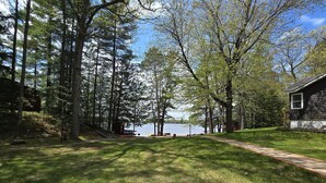 A grassy yard with a wooden deck, a lake view, and a house with a dark exterior. - Shady Rest Cabin #4, Sunset Views, Sandy Beach, Fishing, Trails, Firepit (Rhinelanderi)