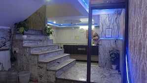 Un hall d’hôtel avec des marches en marbre menant à un comptoir d’accueil, une horloge et un panneau sur le mur.