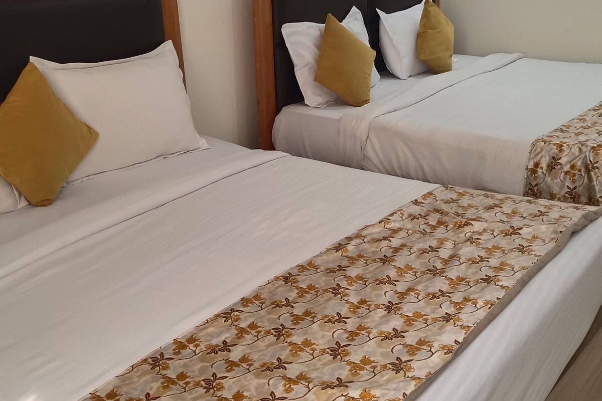 A hotel room with two beds, each with a wooden headboard and white bedding. There is a painting on the wall and a window with curtains.