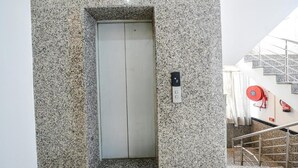 Un ascenseur avec un mur en granit, un enrouleur de tuyau d’incendie et un escalier doté de rampes en métal.