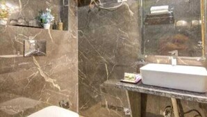 Une salle de bain avec un mur en marbre, des toilettes blanches, un lavabo et un sèche-mains.