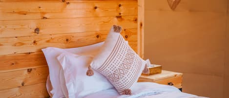 A wooden cabin bedroom with a bed, pillows, and a nightstand.