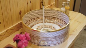 A wooden sauna with a decorative bowl sink, a small vase with pink flowers, and two bottles of soap. - Antares Desert Camp (Merzouga)