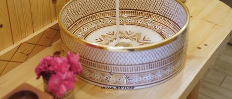 A wooden sauna with a decorative bowl sink, a small vase with pink flowers, and two bottles of soap.