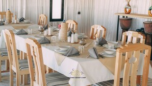 A dining table set with white tablecloth, wooden chairs, and various tableware. - Antares Desert Camp (Merzouga)