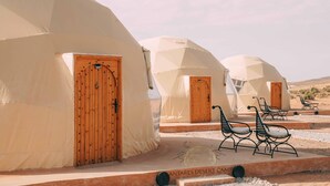 A desert camp with multiple dome-shaped tents, each with a wooden door and a small porch with metal chairs. - Antares Desert Camp (Merzouga)
