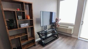 Uma sala de estar com uma estante de madeira, um rack de vidro preto e uma grande janela.