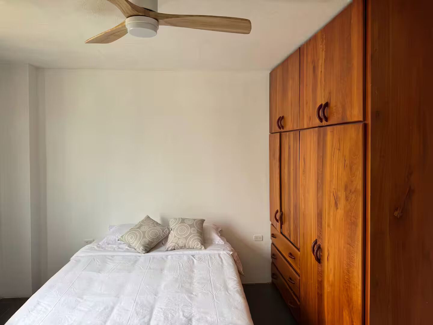 Une chambre à coucher avec un lit, un ventilateur de plafond et une armoire en bois.