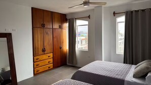 Een slaapkamer met een bed, een kledingkast, een plafondventilator en ramen.
