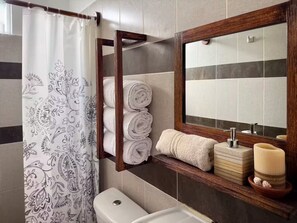 Ein Badezimmer mit Duschvorhang, Toilette, Spiegel und Ablagefläche mit Handtüchern und Toilettenartikeln.