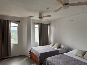 Ein Zimmer mit zwei Betten, einem Deckenventilator und einem Fenster mit Vorhängen.