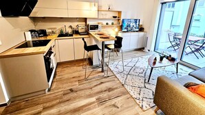 Une cuisine moderne avec des meubles blancs, un coin repas avec une table et des chaises, et une grande porte-fenêtre coulissante donnant sur une terrasse extérieure.