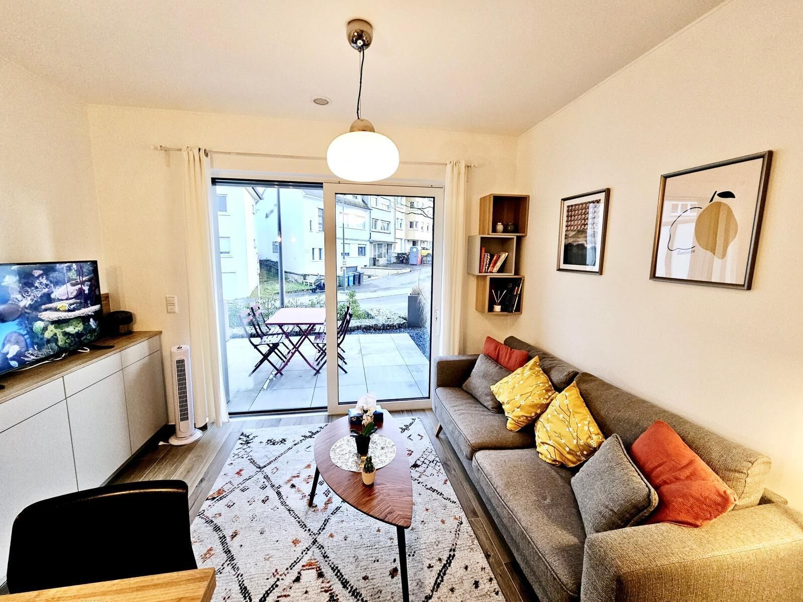 A modern living room with a television, sofa, coffee table, and a view of the street through large glass doors.