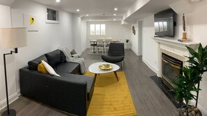 Een moderne woonkamer met een zwarte bank, een geel vloerkleed, een witte salontafel en een open haard.