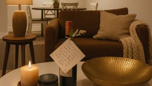 Een gezellige woonkamer met een bruine bank, een ronde tafel met een kaars, een vaas met bloemen en een schaal.