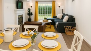 Een moderne woonkamer met een bank, een eettafel voor vier personen, een open haard en een groot raam met gordijnen.